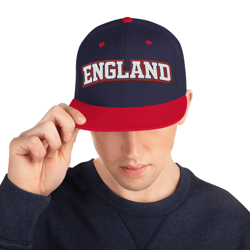 Model wearing navy snapback hat with embroidered England logo and red brim